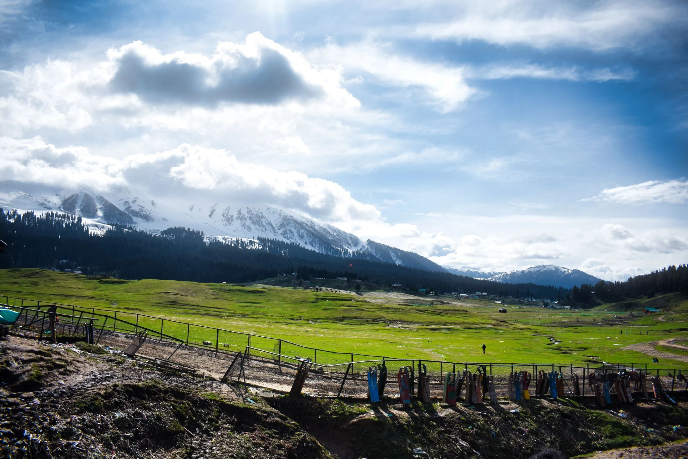 Green meadow in Betaab Valley with snow-streaked mountains and clouds