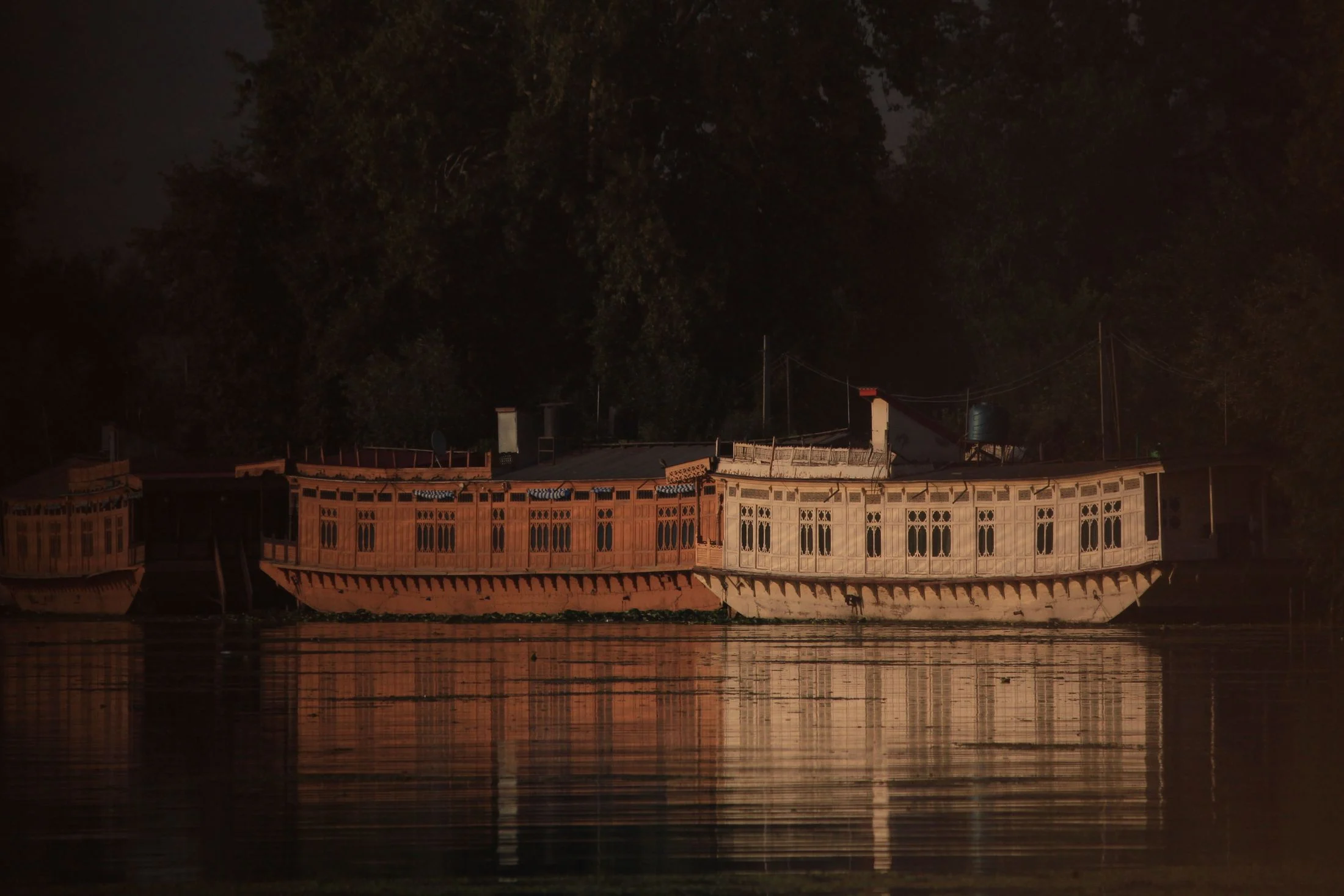 A lit houseboat reflected in dark water at night