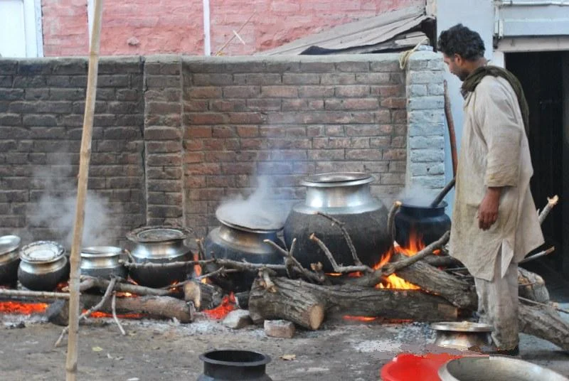A waza tending copper pots of wazwan over a wood fire