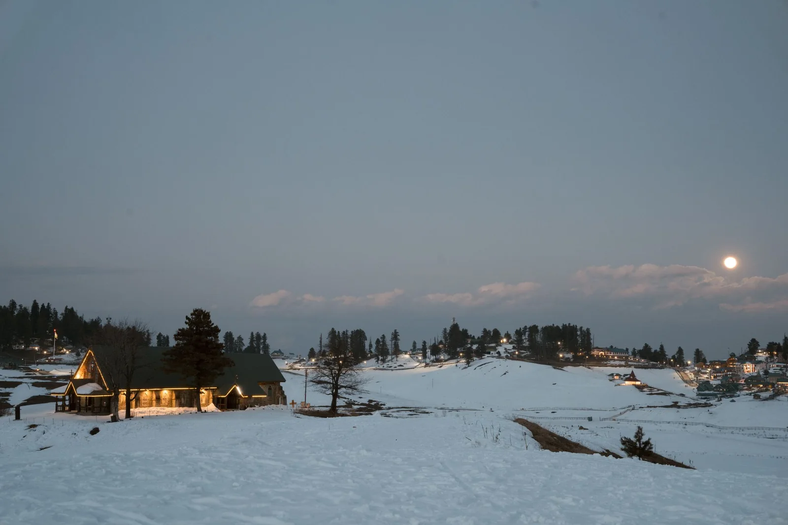 A warmly lit cottage in a snowy Gulmarg meadow at twilight