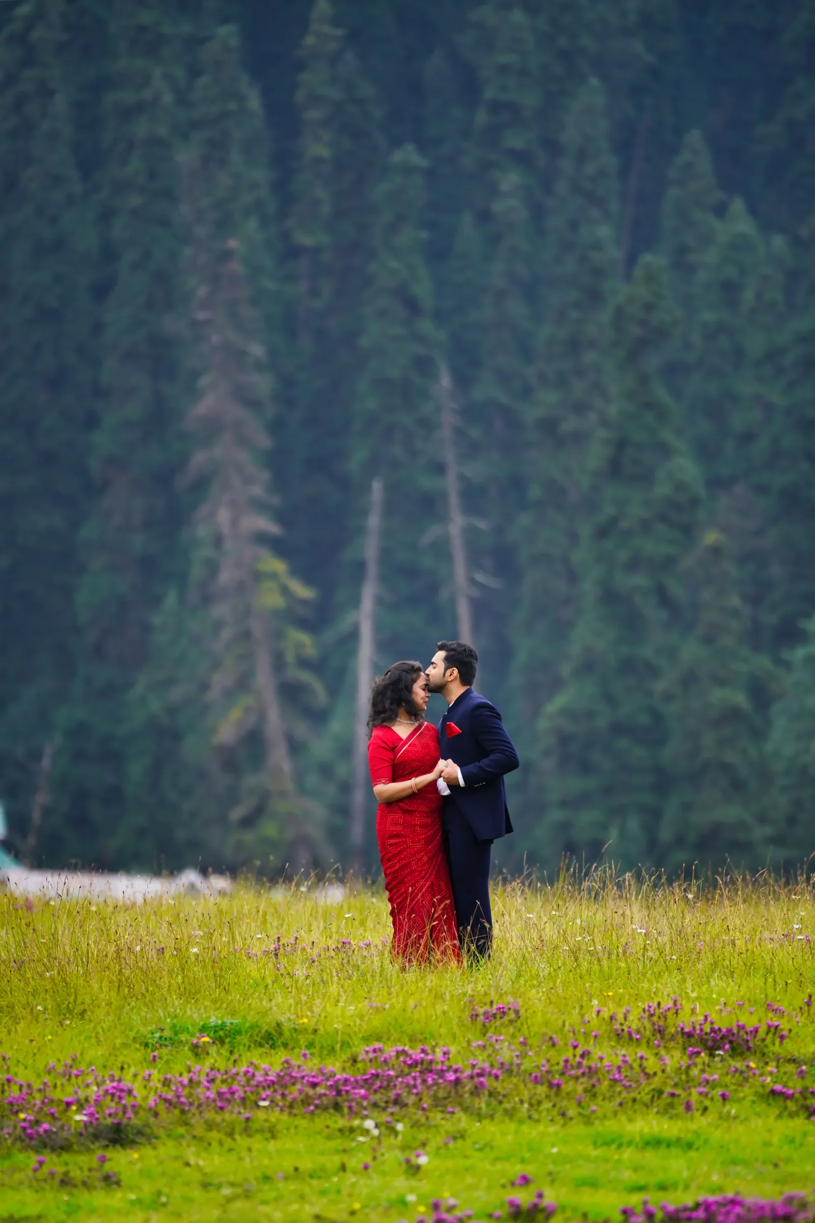 A couple in a flowered meadow beneath a forested Kashmir hillside